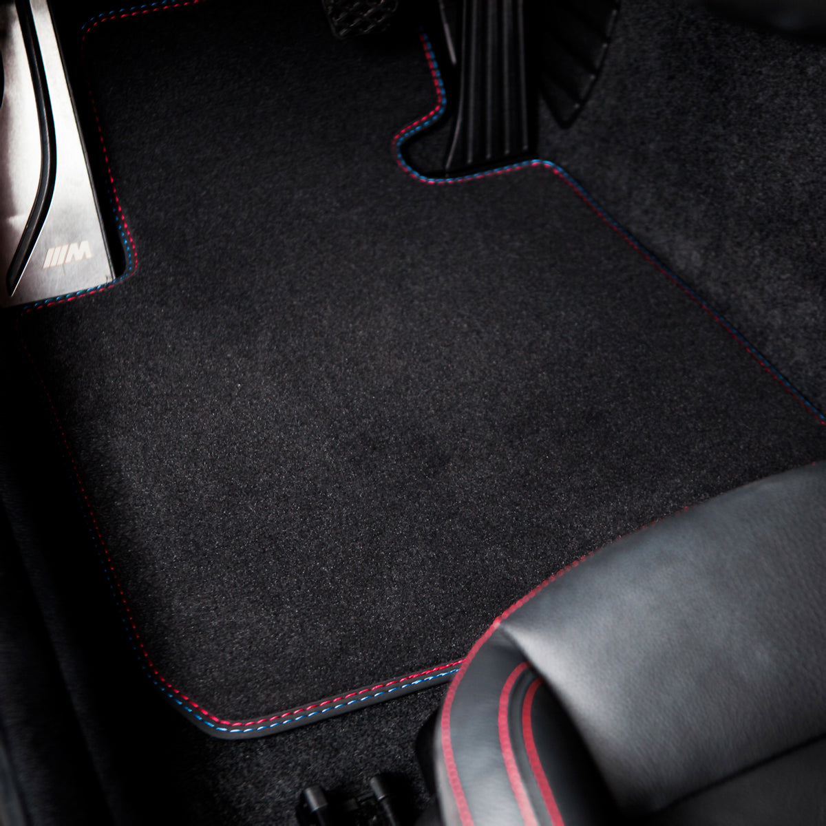 Car floor mat with red stitching on a black car interior